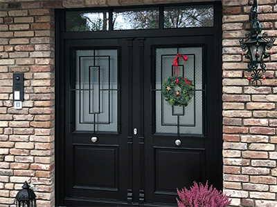 Moderne, maßgefertigte Haustür mit Glasdesign und Weihnachtsdekoration, eingebaut in eine Backsteinfassade.
