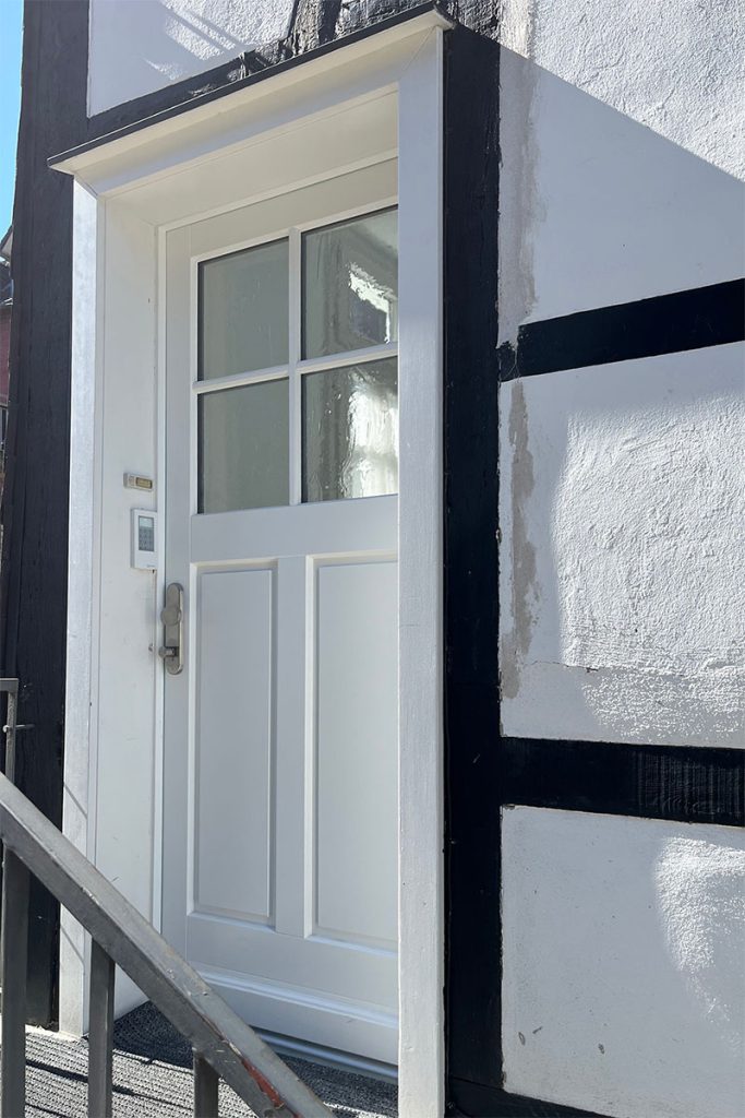Haustüre montiert in einem Fachwerkhaus. Haustüre aus Holz unten mit zwei Füllungen oben mit Licht,ausschnitt und Kreuzsprossenrahmen. Türe weiß lackiert. Verglasung Ornamentglas altdeutsch K. Sicherheitsbeschlag in Edelstahl.