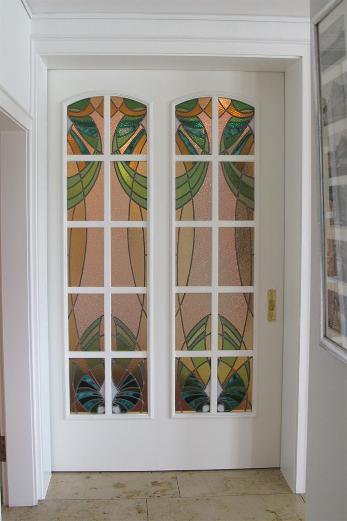 Raumhohe Schiebetüre mit zwei verglaste Feldern. Verglasung im Jugendstil mit buntem Glas und Bleieinfassung. Türblatt und Rahmen weiß lackiert.