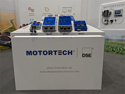 Produkt Display mit schrägen Aufsatz gefertigt aus weißer Möbelplatte vorne mit Firmen Logo bestückt mit Steuerungsmodule. Raum zwischen Aufsatz und Seiten, indirekt beleuchtet mit LED Licht. Das Display steht auf einem Messestand. Im Hintergrund sind die Stand Wände zu sehen.