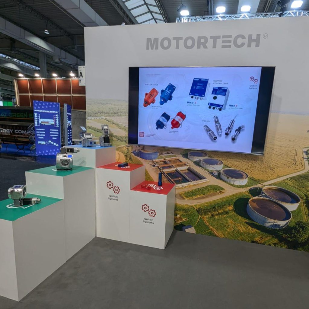 Blick auf einen Messestand. Im Hintergrund steht eine Messewand mit einem großen Bildschirm. Daneben stehen fünf Displays in in unterschiedlichen Höhen wie eine Treppe. Die Displays sind weiß teilweise mit rotem und grünen Print.